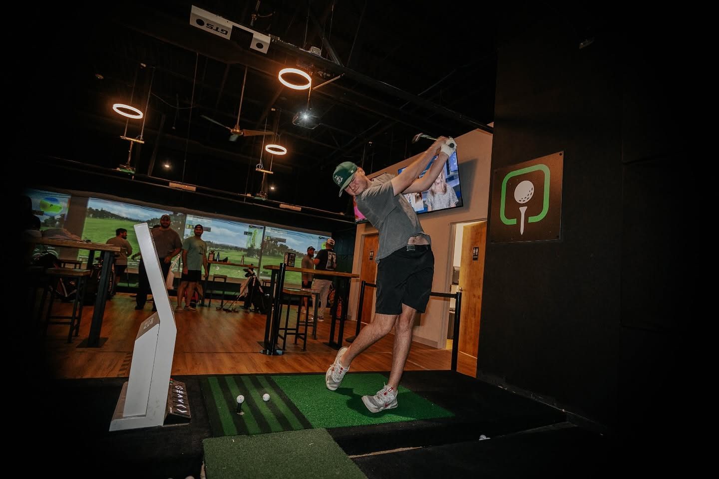 Golfer mid-swing in a bay, screen visible behind